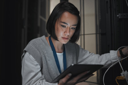 Tablet, server room and communication with a programmer asian woman at work on a computer mainframe. Software, database and information technology with a female coder working alone on a cyber networkの写真素材