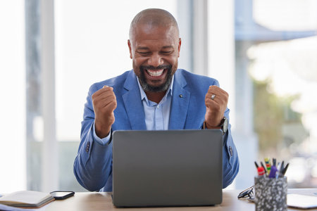 Happy black man, laptop and celebration for winning, sale or good news on discount at the office desk. Excited African American male celebrating on computer for promotion, bonus or achievementの写真素材