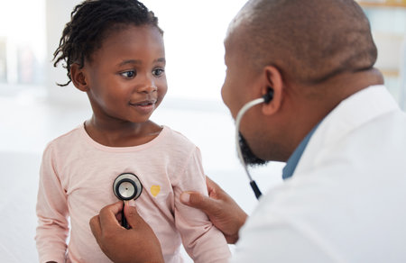 Healthcare, pediatrician and child heart doctor with a patient at hospital, exam on chest with a stethoscope. Black girl smile at pediatric surgeon, talking to a friendly, caring physician she trustの写真素材