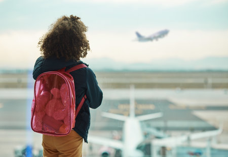 Girl child, looking and airport window for greeting, goodbye and focus for airplane, international transport or travel. Kid, back and watch takeoff by glass for global immigration, young and Africanの写真素材