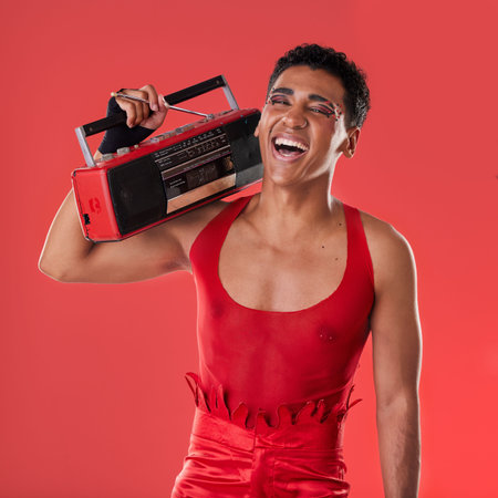 Happy, man and boombox radio in studio for gay, pride and vogue aesthetic with retro 80s tech by red background. Lgbtq model, vintage fashion and music with happiness, listening and comic laughingの写真素材