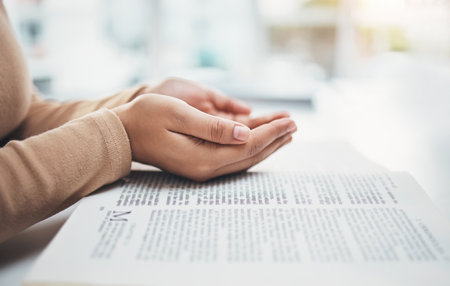 Religion, prayer and bible with hands of woman for worship, support and Christian faith. Believe, spirituality and God with girl praying over catholic holy text for wellness, respect and hopeの写真素材