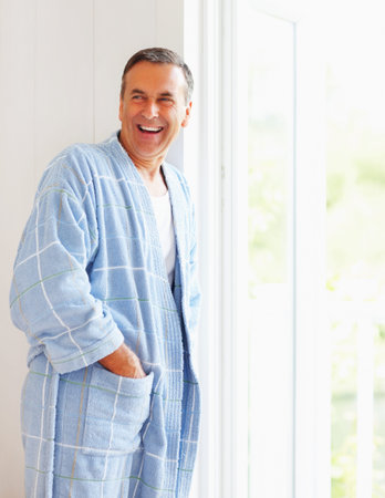 Mature man wearing bathrobe while leaning against wall. Portrait of a cheerful mature man wearing bathrobe while leaning against wall.の写真素材