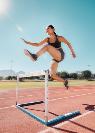 Fitness, hurdle and woman running in stadium track for training, health and sports workout. Exercise. cardio and endurance with strong girl runner and jump for power, performance and competitionの写真素材