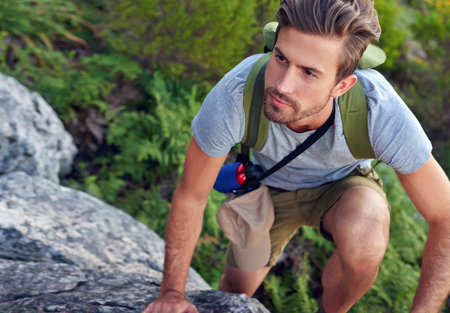 Making his way to the top. a handsome young man scaling a mountain.の写真素材