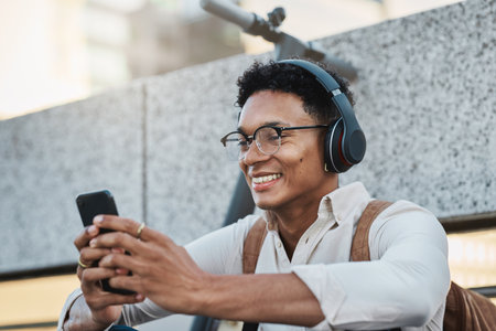 Music, phone and city with a business black man streaming or listening to music while networking. Schedule, mobile and street with a male employee using headphones to stream audio in an urban townの写真素材