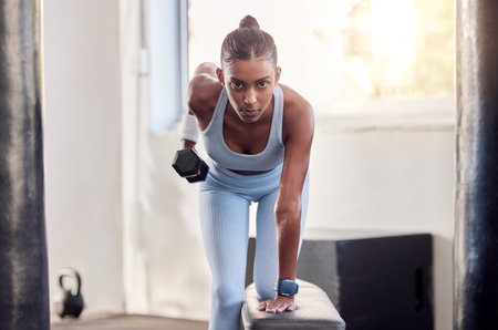 Fitness, dumbbell weight and black woman doing a workout for strength, health and wellness in a gym. Motivation, athlete and healthy African girl doing an arm exercise or training in a sports center.の写真素材