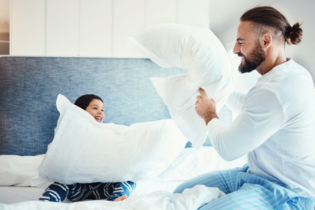 Happy, love and father in pillow fight with his child on the bed in the bedroom of family house. Happiness, smile and dad being playful with his boy kid while bonding, playing and having fun at home.の写真素材