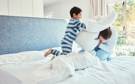 Playing, dad and son in pillow fight on bed, fun quality time and man bonding with child at home. Smile, happy and play, father and kid in bedroom with pillows, joy and happiness together on weekend.の写真素材