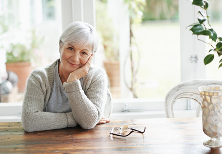 Pleased with the life shes created. A senior woman sitting at her kitchen table smiling at the camera.の写真素材