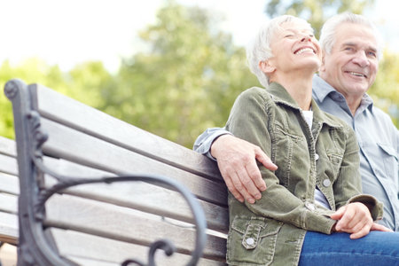 Enjoying a day at the park. A mature couple sitting on a bench in the park and laughing together.の写真素材