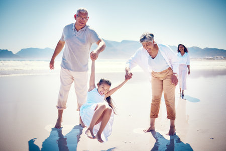 Beach, family holding hands and grandparents with kid playing and walking on ocean sand together. Fun, vacation and happy senior man and woman with children bonding, quality time and summer in natureの写真素材