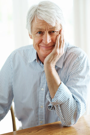 Looks like dinner for one. Portrait of senior man sitting indoors while smiling at the camera.の写真素材