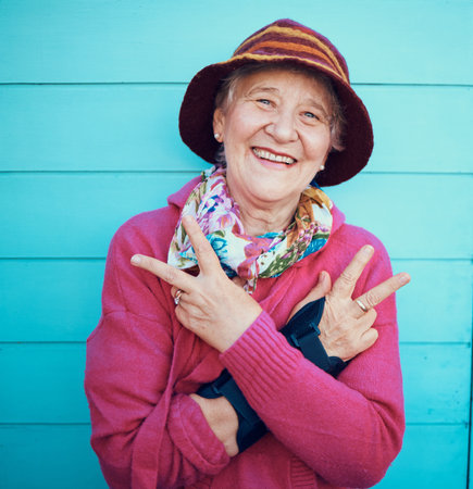 Peace sign, hip hop and portrait of a senior woman in the city with energy, smile and urban fashion. Cool, trendy and elderly grandma with emoji hand in retirement on a blue background or wallの写真素材