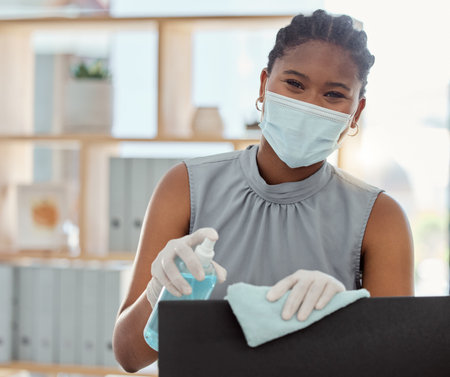 Covid, mask and sanitizer with a business black woman cleaning her computer and office equipment at...