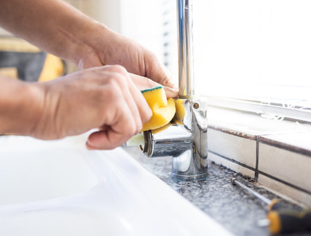 Plumber man, tap and hands of maintenance for sponge, home renovation and builder service. Closeup handyman, sink and plumbing installation in house, engineering contractor or upgrade pipeline systemの写真素材
