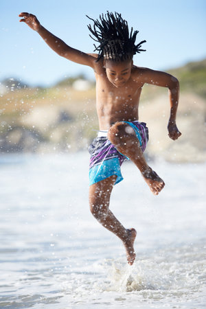 Splash. An excited young boy leaping into the air while at the beach.の写真素材