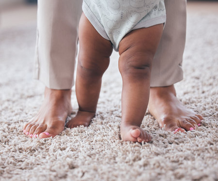 Baby feet, youth walking and kid learning with mother in living room lounge with mobility development. Floor, home and first steps of a young child with mama love, care and support in a houseの写真素材