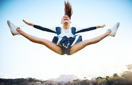 Cheerleader woman, sky and sports performance with smile and energy to celebrate outdoor. Cheerleading person dance or jump stunt while laughing with joy for training workout, freedom or competitionの写真素材