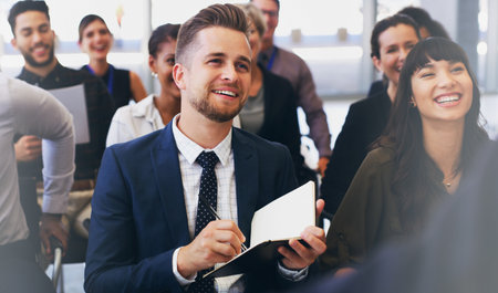 Please repeat that so I can make a note. Cropped shot of a handsome young businessman sitting with his colleagues and holding a notebook while in the office.の写真素材
