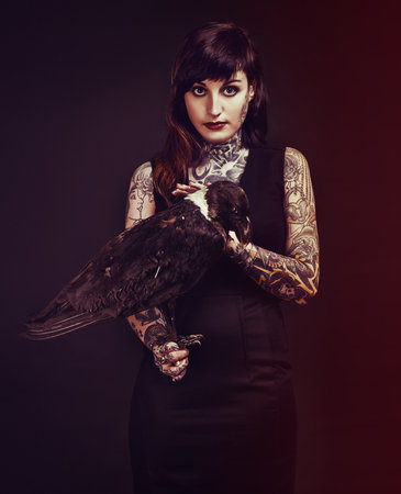 Enigmatic Temptress. Studio shot of a tattooed young woman holding a bird.の写真素材