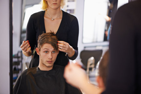 Hes going for a new style this time. a young man having his hair styled by a hairdresser.の写真素材