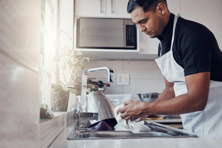 Cleaning kitchen, washing dishes and a man in house, home or apartment to clean for safety from bacteria. Male cleaner person at sink with a cloth in hands for hygiene and a healthy lifestyleの写真素材