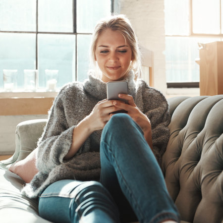 Woman, sofa and smartphone on social media, reading or communication on internet to relax in lounge. Girl, couch and chat with phone, mobile tech or online dating for partner, love or romance in homeの写真素材