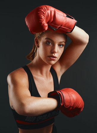 You can do just about anything with determination. Studio portrait of a sporty young woman wearing boxing gloves against a black background.の写真素材
