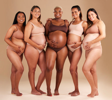 Pregnancy, diversity and portrait of friends in studio for community, motherhood and prenatal wellness. Maternity, love and pregnant women showing their baby bump stomach together by beige backgroundの写真素材