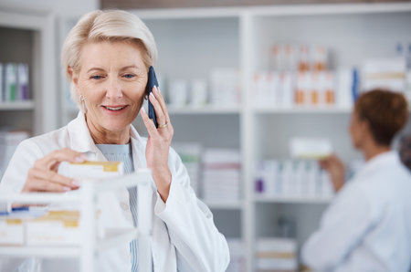 Pharmacy medicine, pharmacist phone call and woman talking in drugstore for telehealth. Healthcare, smartphone and happy senior medical doctor in consultation for medication prescription in shop.の写真素材