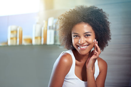 Give your face something to smile about. Cropped portrait of a young woman moisturizing her face in the bathroom.の写真素材
