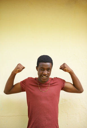 On the road to manhood. a teenage boy showing off his muscles while standing against a wall.の写真素材