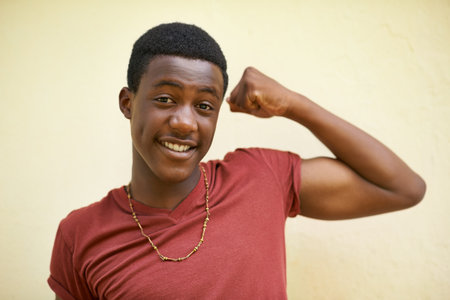 Watcha think. Portrait of a teenage boy showing off his muscles while standing against a wall.