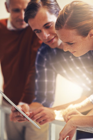 Sharing technology and ideas. three coworkers talking over a digital tablet while standing in a stairwell.の写真素材