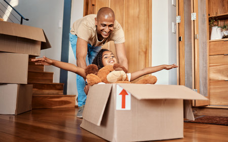 New home, father and pushing girl in box, having fun and bonding after moving in house. Real estate, family property and child with teddy bear, boxes and happy dad playing to celebrate relocation.の写真素材