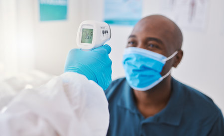 Checking for covid, corona or fever with a patient wearing a mask for hygiene, sickness or flu symptoms in a health clinic. Medical doctor holding a thermometer to scan the temperature of a patientの写真素材