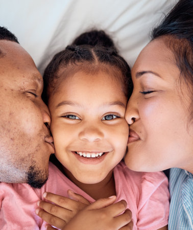 Parents kiss, daughter and smile portrait of a black family together with love, bonding and care. Home, happiness and youth of a kid, mother and father top view cheek kissing a face on a bedroom bedの写真素材