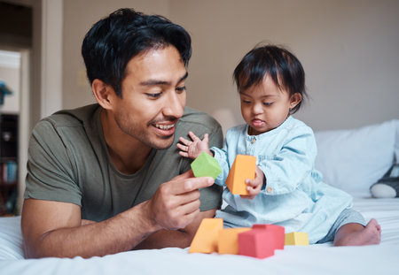 Baby, down syndrome and learning on a bed with child and father playing with educational blocks in a bedroom. Family, disability and kids bonding with asian parent, relax with creative activityの写真素材