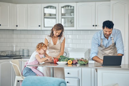 Kitchen, cooking and family with laptop with vegetables, food nutrition information and internet recipe search for healthy, vegan lifestyle. Parents and child learning together for lunch or dinnerの写真素材