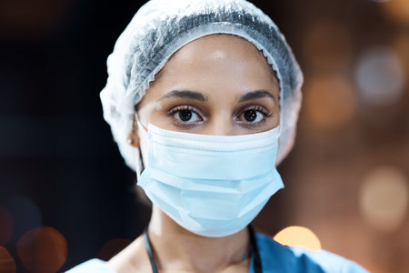 Woman, doctor and portrait with face mask in night at workplace, hospital and career vision on nightshift by window. Healthcare expert, dark clinic and focus goal with ppe, safety and stop covid 19の写真素材