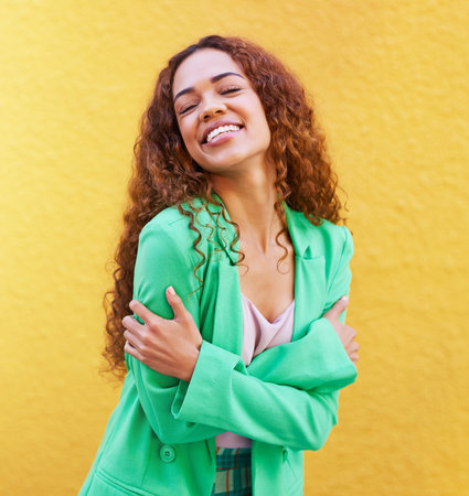 Black woman, fashion and self love on yellow wall background for motivation, beauty and style. Gen z Colombia person with curly hair outdoor for freedom, hug and positive mindset for trendの写真素材