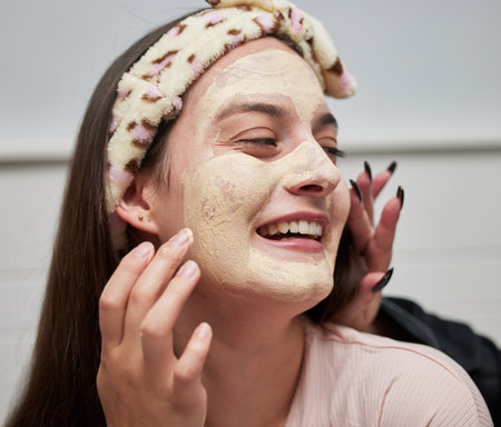 Sleepover, face mask and skincare of a young woman happy about facial and wellness in a bedroom. Friends, lotion and dermatology treatment of youth together having fun doing skin care for glowの写真素材