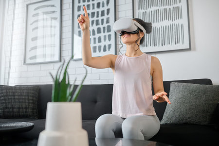 Virtual reality, metaverse and gaming with a woman in the living room of her home using a headset to...
