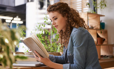 Take your hobbies wherever you go. a young woman reading a book in a coffee shop.