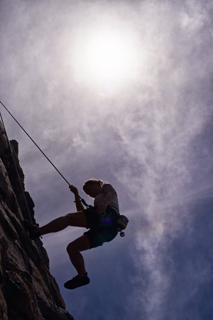 The courage of a rock climber. A silhouette of a young woman abseiling down a rock face.の写真素材