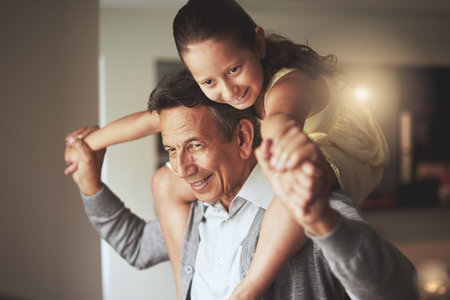 Having so much fun with her grandpa. a grandfather giving his granddaughter a piggyback ride at home.の写真素材