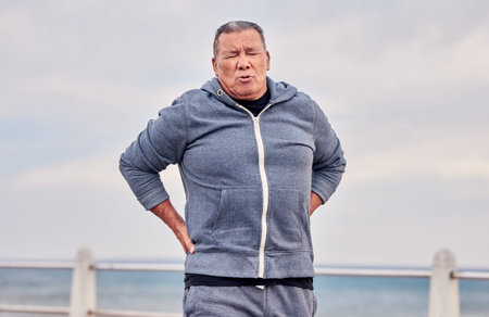 Back pain, fitness and senior man outdoor at beach with scoliosis, sports wound and risk. Male...