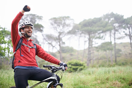 Pure exhilaration. A young male athlete pumping his fist in the air after conquering a mountain biking trail.の写真素材