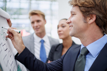 Revising their business strategy. A businessman drawing a diagram on a flip-chart as his colleagues stand by.の写真素材